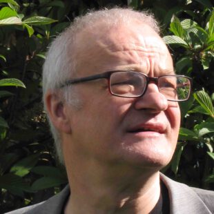 Porträt-Foto des Herausgebers Bruno E. Landthaler im leichten Profil, vor einer Blätterwand