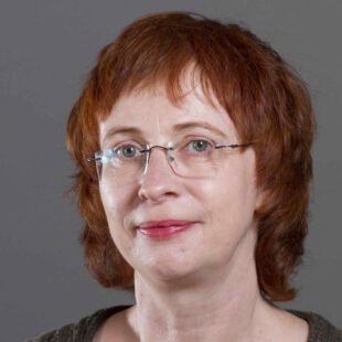 Porträt-Foto der Herausgeberin Hanna Liss. Liss hat einen roten Kurzhaarschnitt und trägt einen rahmenlose Brille