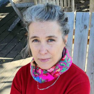 Orit Bergmann Porträt-Foto der Autorin Orit Bergmann in einem Holzstuhl. Bergmann trägt einen roten Pullover und einen bunten Schal.